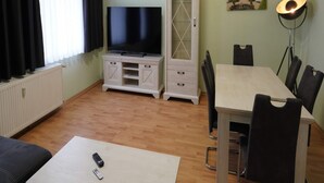A living room with a TV, a cabinet, a dining table with chairs, and a lamp. - Ferienwohnung Otto der Reiche in Ballenstedt (Ballenstedt)