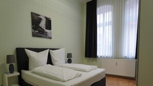 A bedroom with a bed, two bedside tables, a wall-mounted picture, a window with curtains, and a radiator. - Ferienwohnung Otto der Reiche in Ballenstedt (Ballenstedt)