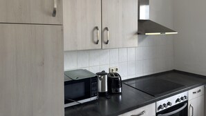 Eine moderne Küche mit hellen Holzschränken, einer schwarzen Arbeitsplatte, einer eingebauten Mikrowelle, einem Toaster und einem Herd.