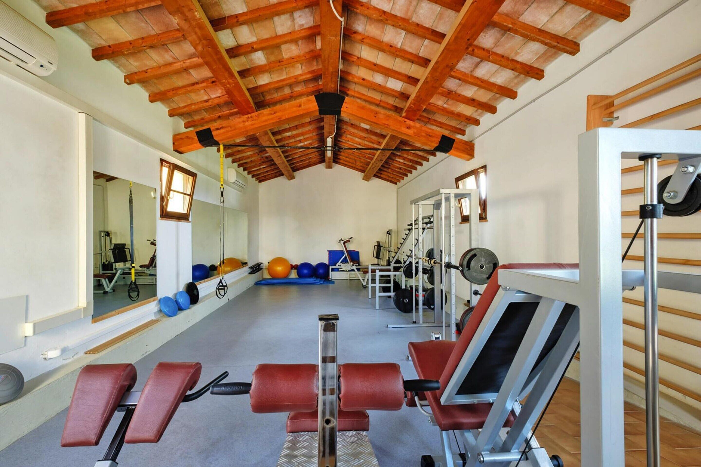 Un gimnasio con vigas de madera en el techo, equipo de ejercicio y un espejo grande.