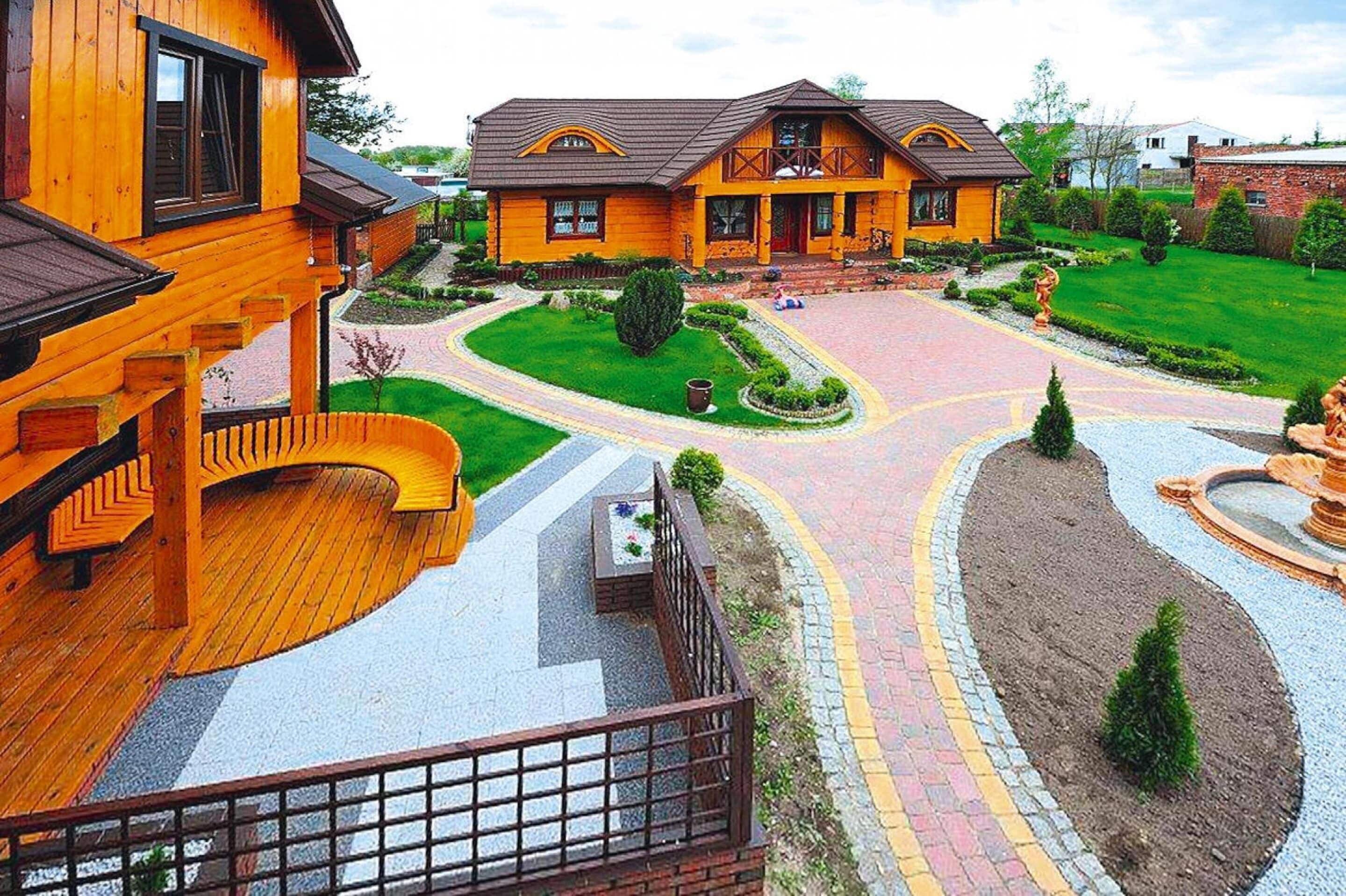 A two-story wooden house with a landscaped garden and a curved driveway.