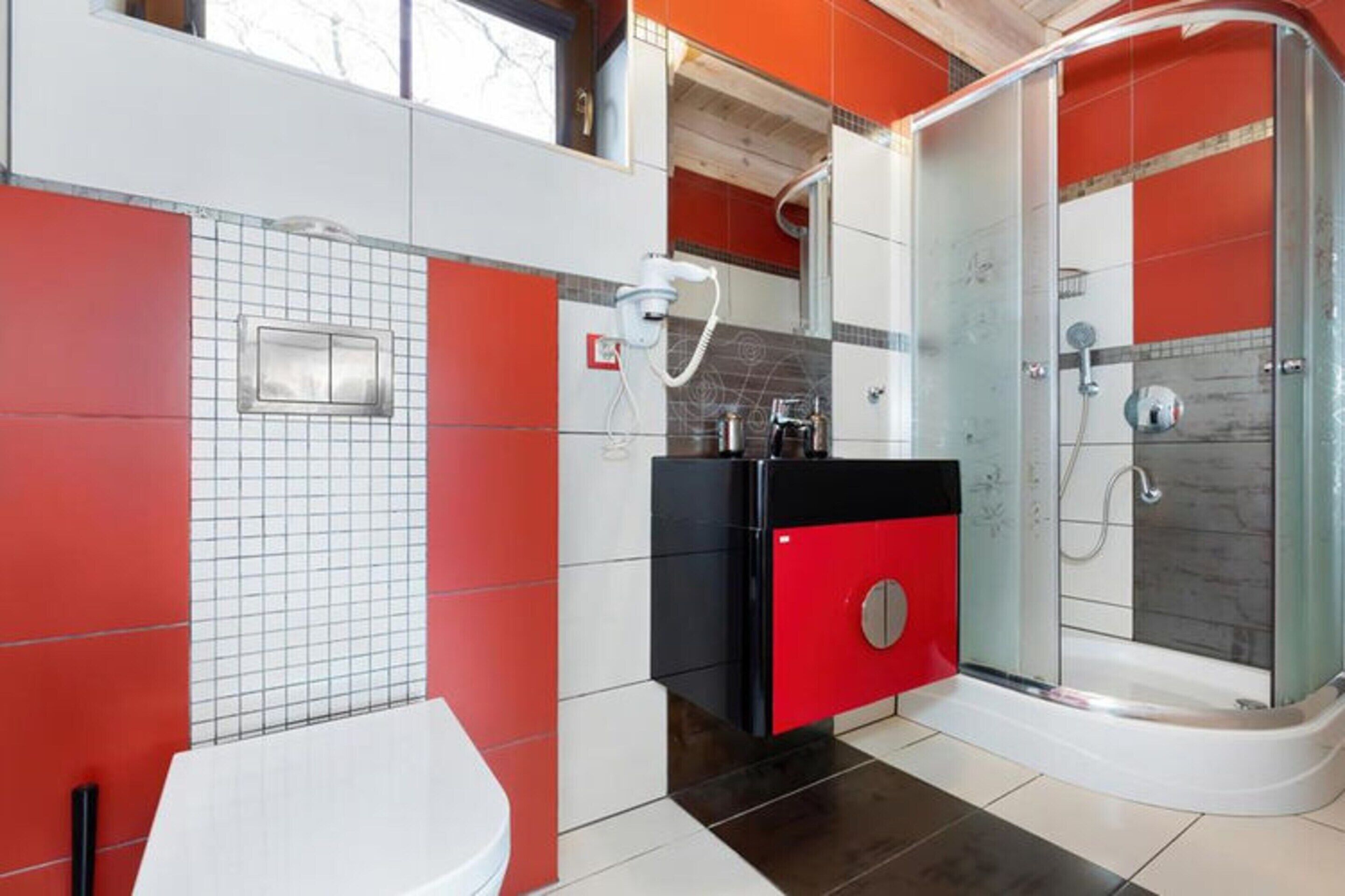 A modern bathroom with a glass-enclosed shower, a red cabinet, and a white toilet.