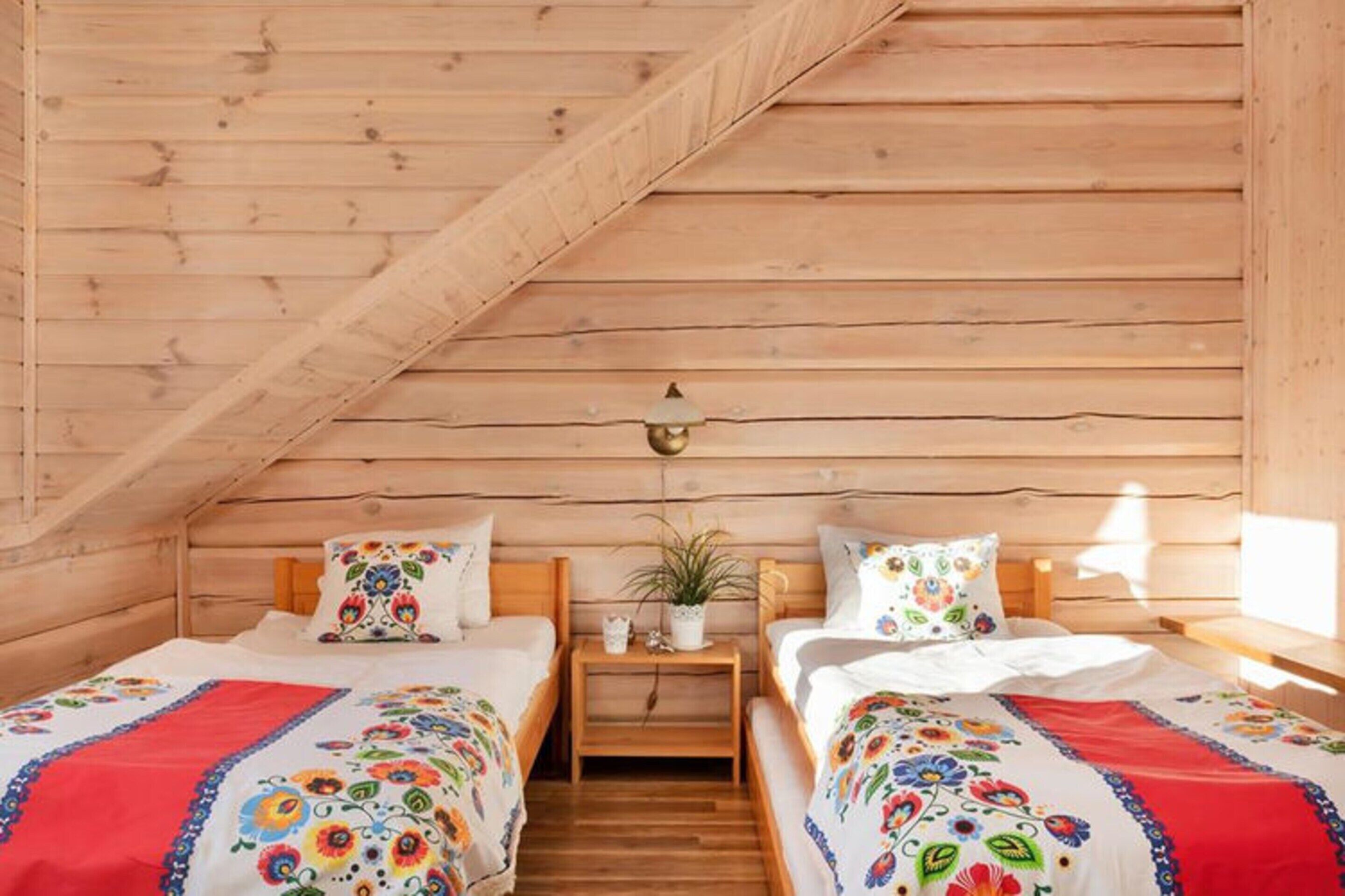 A cozy attic bedroom with two beds, wooden walls, a sloped ceiling, and a small bedside table with a lamp.