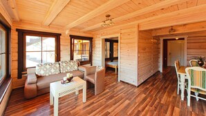 A log cabin interior with a wooden floor, a sofa, a dining table with chairs, and a ceiling with wooden beams. - Comfortable Holiday Home Close to the Beach (Ustronie Morskie)