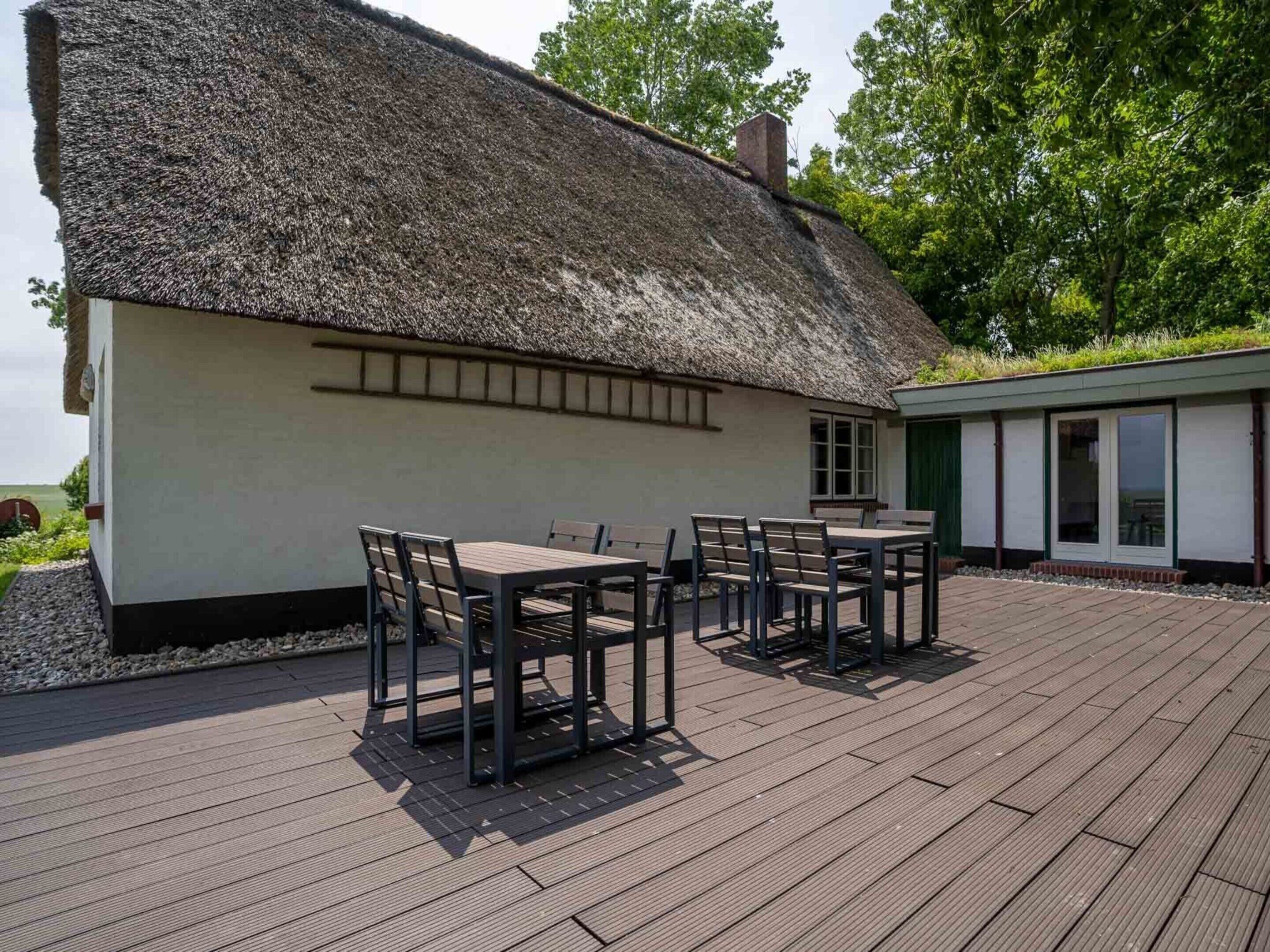 Une maison à toit de chaume dotée d’une terrasse en bois et d’un espace salon extérieur.