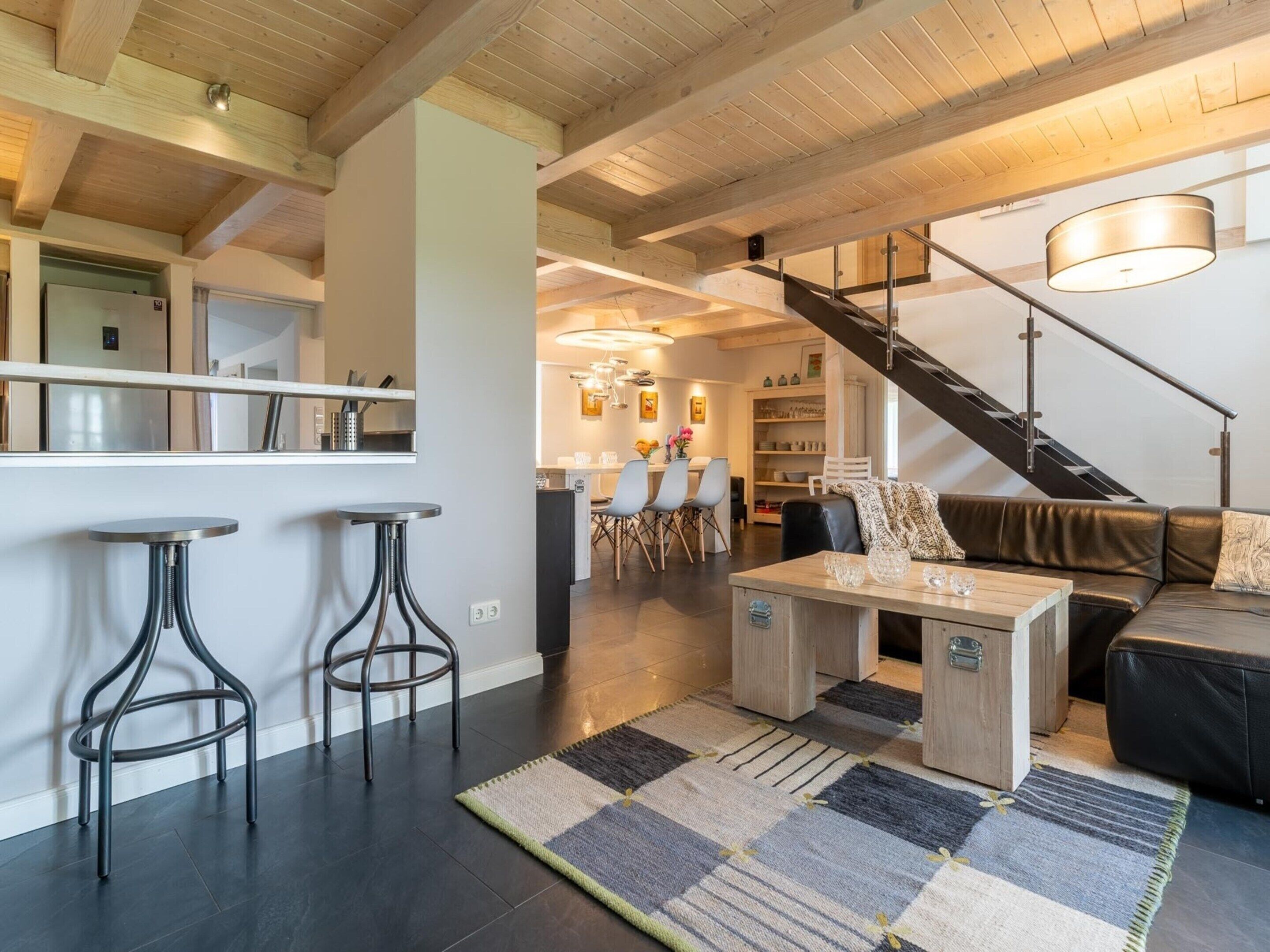 Ein modernes Wohnzimmer mit einer Couch, einem Couchtisch und zwei Barhocker. Eine Treppe führt auf eine erhöhte Ebene.