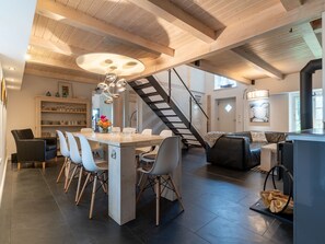 A modern kitchen with a central island, a dining area with chairs, a staircase, and a living area with a sofa. - Reetgedecktes Ferienhaus in Westerhever mit Sauna (Westerhever)