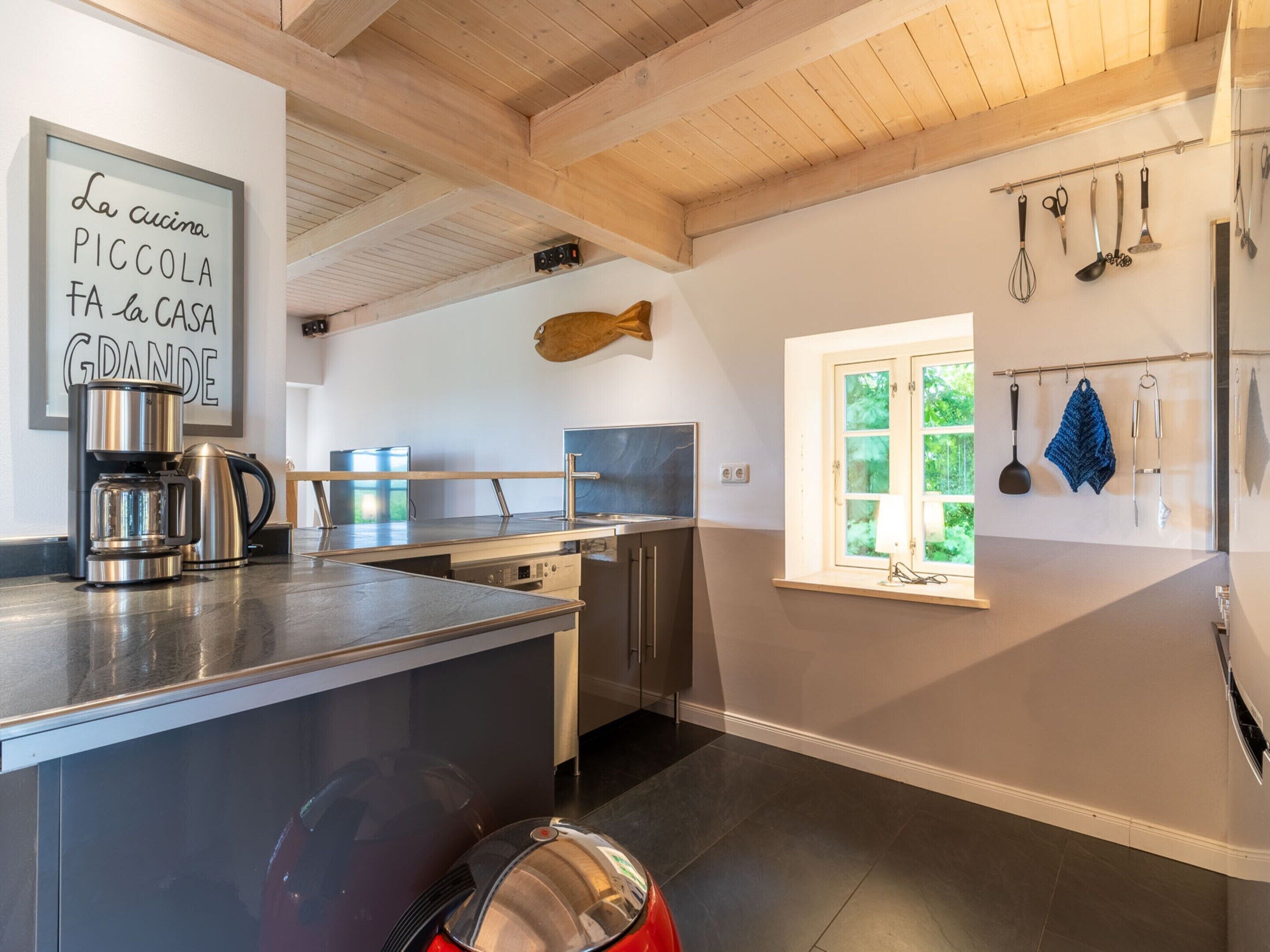 A modern kitchen with a coffee machine, a dishwasher, and a window with a view of greenery.