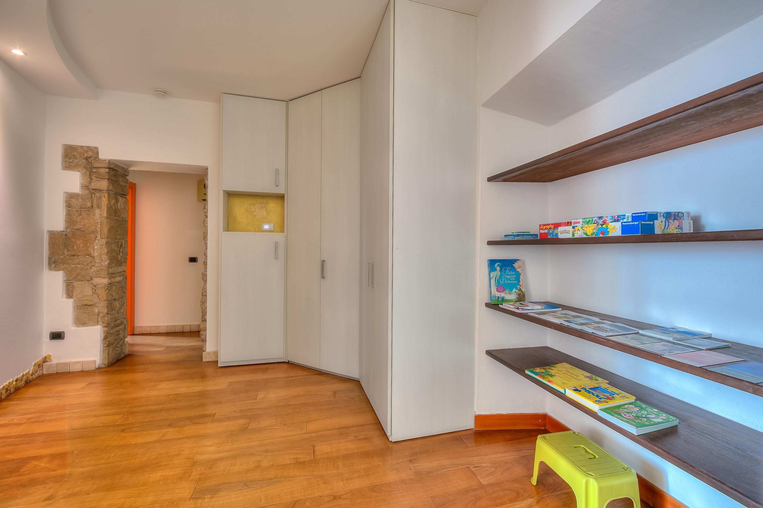 A room with wooden flooring, white walls, a stone accent wall, a bookshelf with books, and a yellow stool.