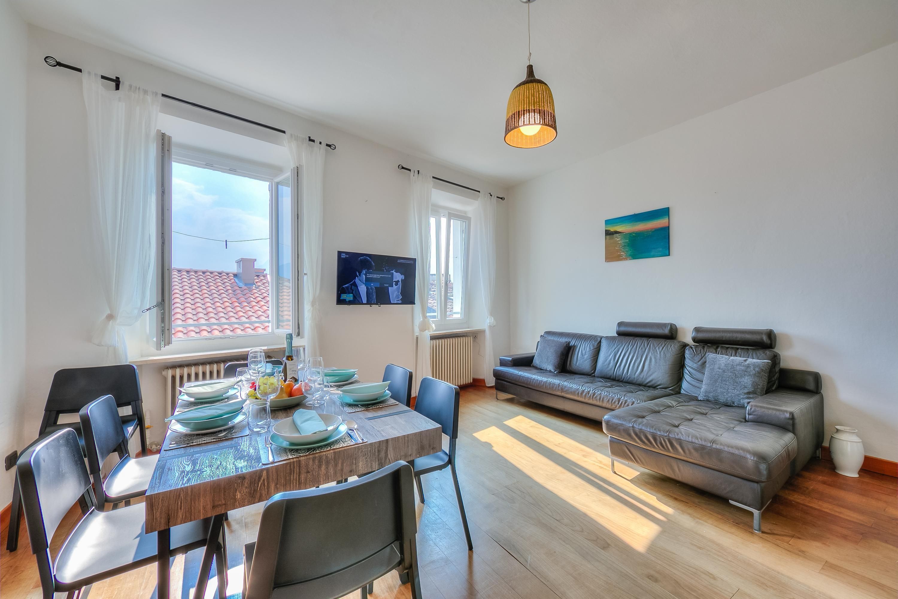 Ein modernes Wohnzimmer mit Essbereich, einem grauen Sofa und einem Fernseher an der Wand.