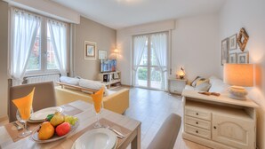 A hotel room with a dining area, a bed, a TV, and a bedside table with a lamp. - Elena Apartment - Family Friendly (Salò)
