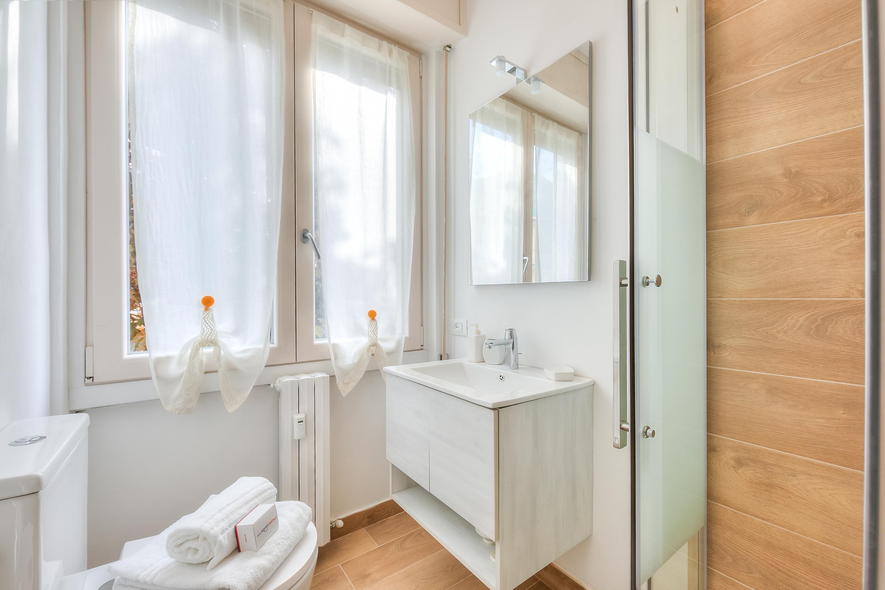 Ein modernes Badezimmer mit Waschbecken, Spiegel und Toilette in Weiß. Handtücher liegen auf der Heizung und eine Glasduschtür ist vorhanden.