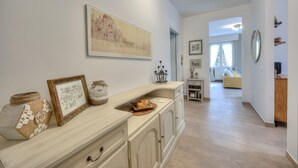 A hallway with a light-colored wooden floor, a white wall with a framed map, and a small table with decorative items. - Elena Apartment - Family Friendly (Salò)
