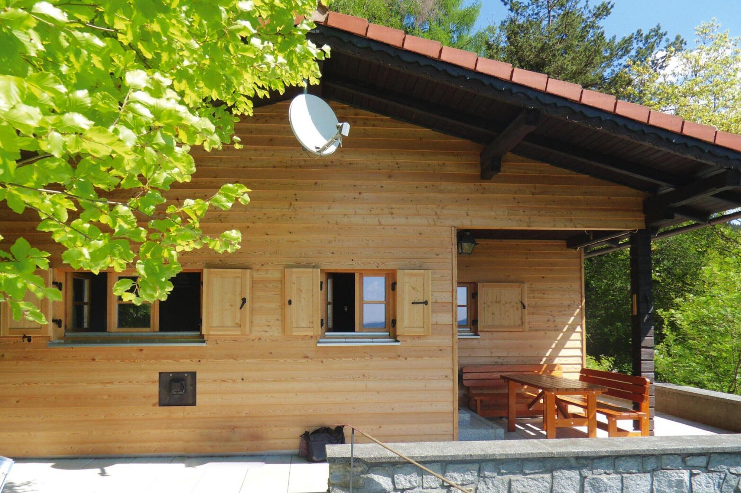 Eine Holzhütte mit Satellitenschüssel, einer überdachten Veranda mit Tisch und Bänken sowie einer Steinmauer.
