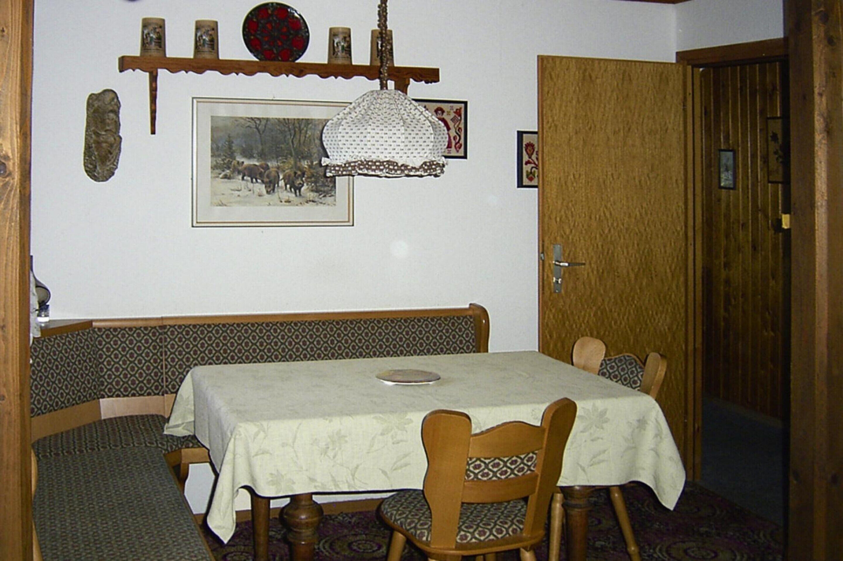 Un coin repas avec une table dressée pour quatre personnes, un banc, des décorations murales à motifs et un tableau encadré accroché au mur.