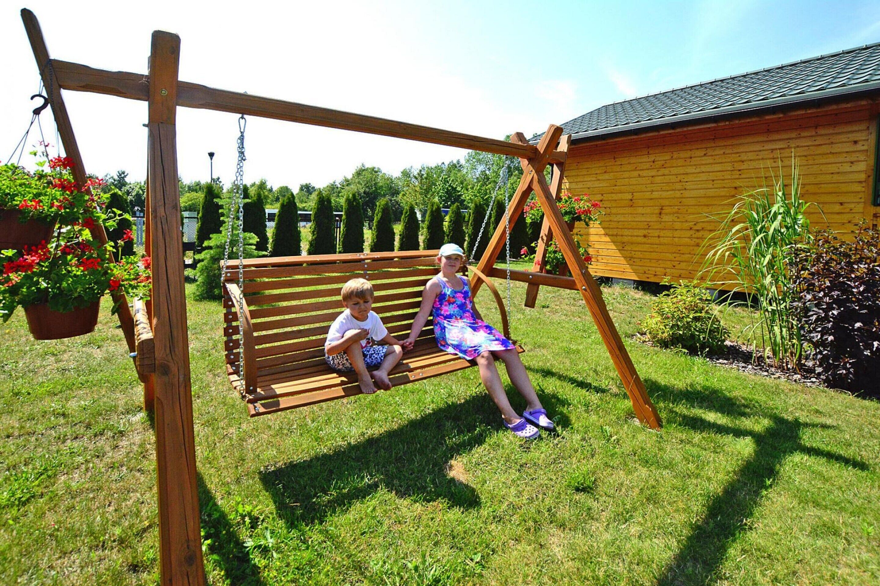 A wooden swing set in a garden with a wooden building in the background.
