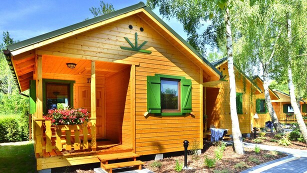 Een houten chalet met een veranda, groene luiken en een kleine tuin.