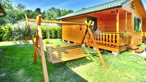 Een houten chalet met een veranda, omringd door een tuin met bloemen en een schommel.