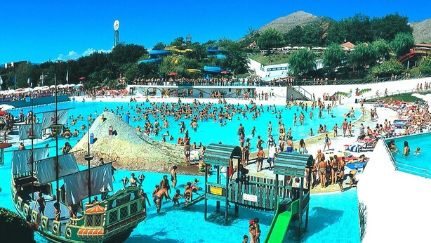 Un'ampia piscina esterna con diverse corsie, una torretta per i bagnini e una barca ormeggiata nelle vicinanze.