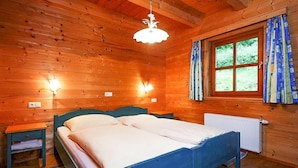 Un dormitorio de cabaña de madera con una cama doble, dos mesitas de noche, un ventanal con cortinas y un radiador.