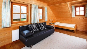 Una cabaña acogedora de madera con un sofá de cuero negro, una cama de madera pequeña y dos ventanas con cortinas.