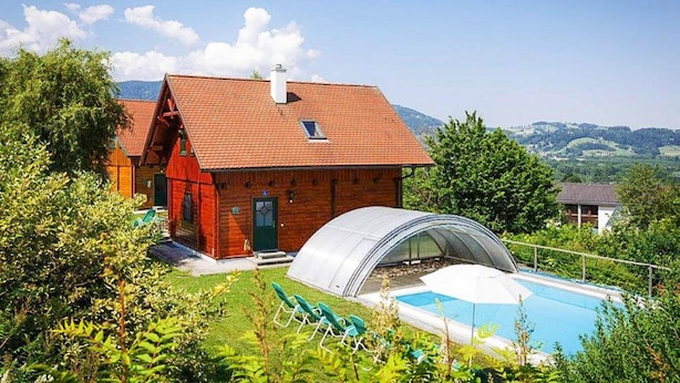 Una casa de madera con techo rojo, piscina e invernadero.