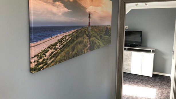 Ein Zimmer mit einem großen Gemälde einer Küstenlandschaft, einem Fernseher auf einem Schrank und einer Tür zu einem weiteren Bereich.