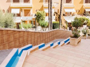 A hotel courtyard with steps leading to a pool area, surrounded by buildings with balconies and potted plants. - Apartment in Pueblo Salado, Mazarron (Mazarrón)
