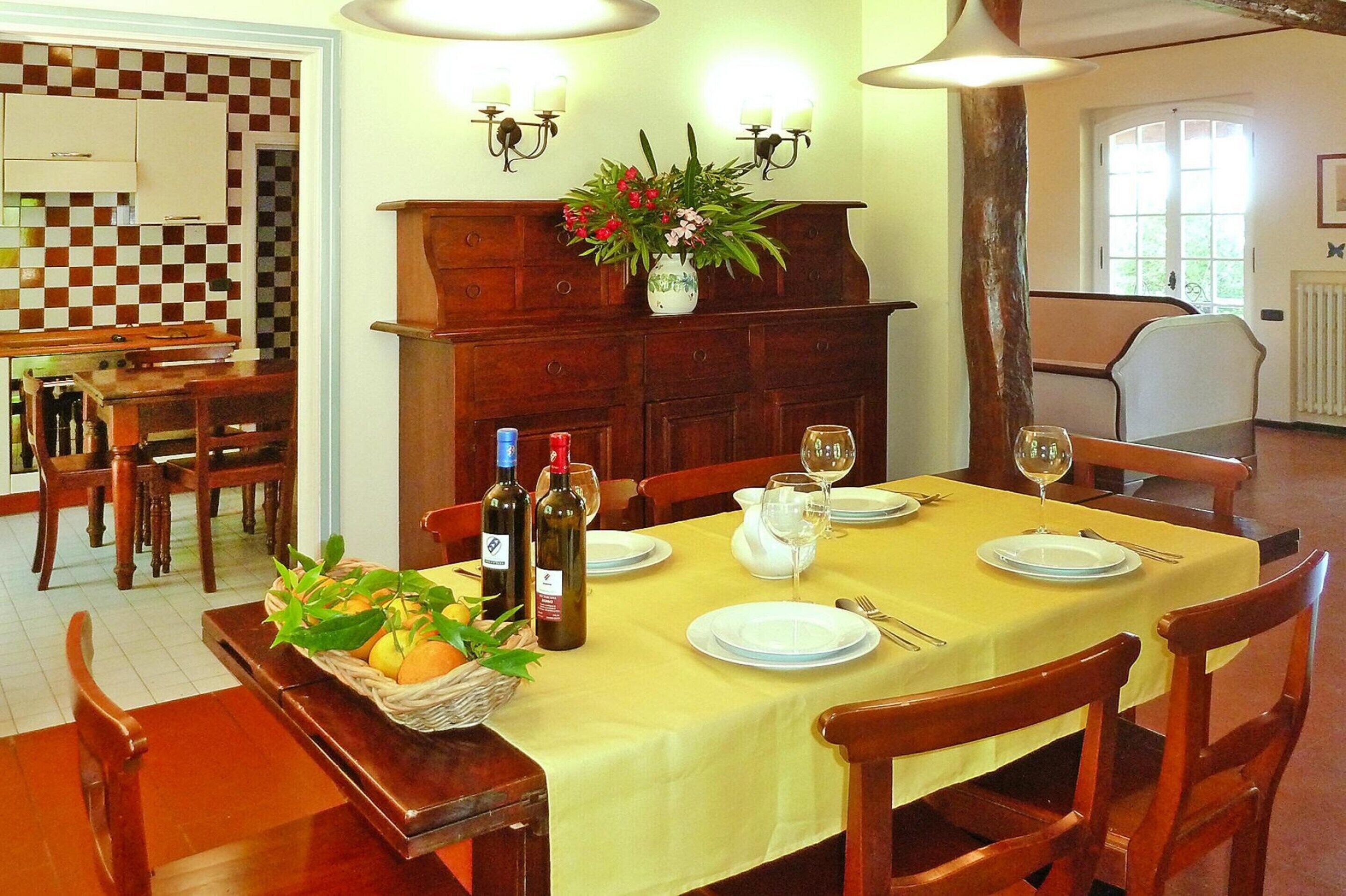A dining area with a table set for four, wooden chairs, a buffet table with fruits, and a vase with flowers.