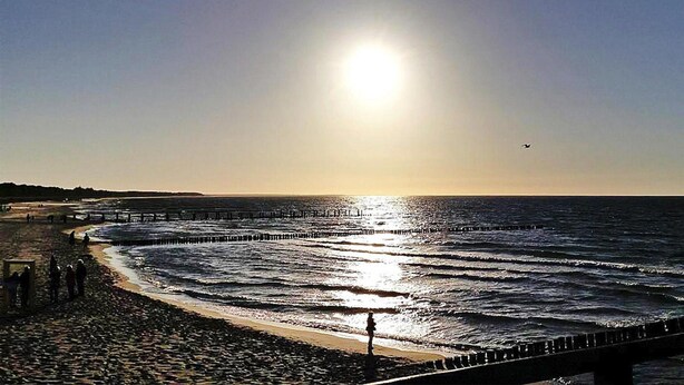 A beach with a pier extending into the ocean, a clear sky, and the sun low on the horizon. - Apartment, Zingst (Zingst)