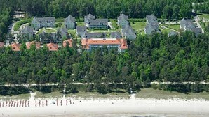 Vista aerea di una zona costiera con numerosi edifici, una spiaggia e una zona boschiva.