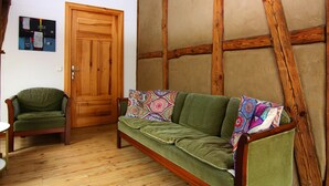 Una habitación con techo de madera, un sofá verde con cojines estampados, una puerta de madera y una pequeña mesa.