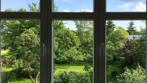 Vista a través de una ventana de varios paneles, mostrando un jardín exuberante con varios árboles y un césped bien cuidado.