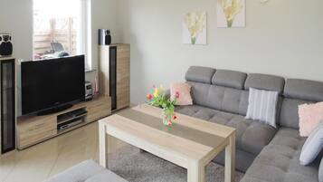 A modern living room with a grey sofa, a wooden coffee table, and a flat-screen TV on a wooden stand.