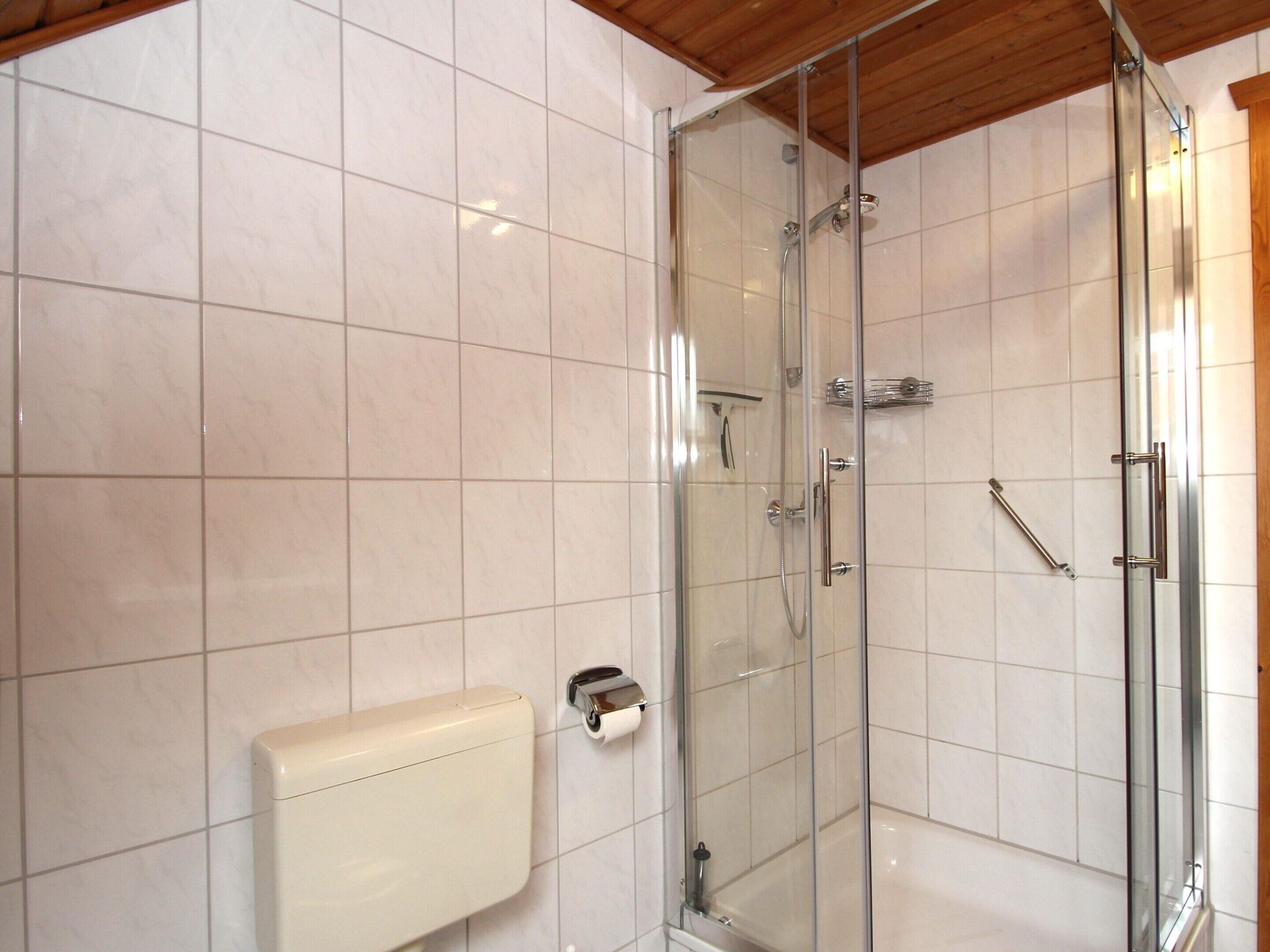 Ein modernes Badezimmer mit einer gläsernen Dusche, weiß gefliesten Wänden und einer Holzbalkendecke.
