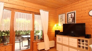 A cozy cabin with wooden walls, a television, a radiator, and a window with curtains. - Doppelhaushalfte in Hasselfelde (Oberharz am Brocken)