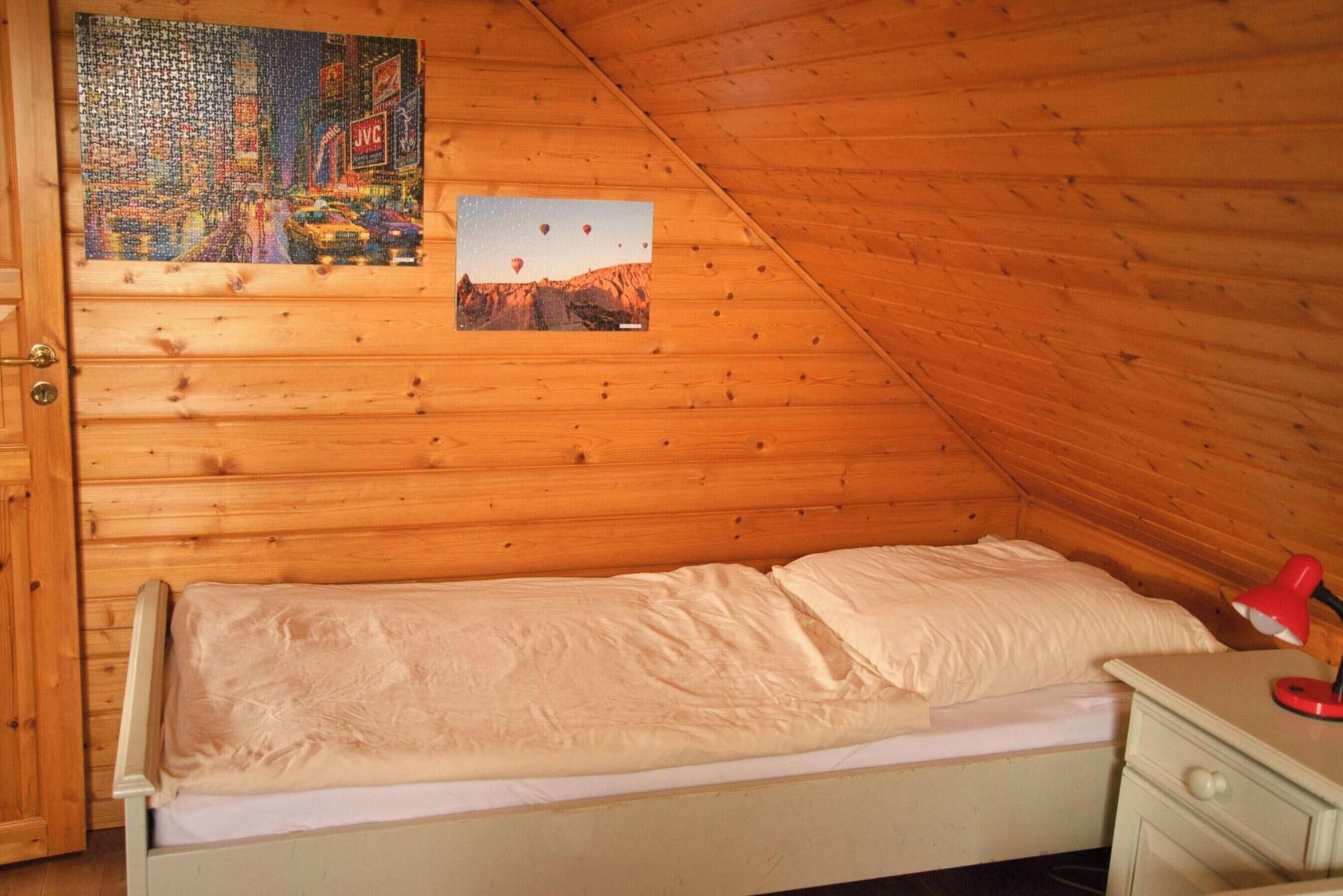 Un lit simple dans une pièce aux murs en bois, une petite table de chevet et une lampe rouge.