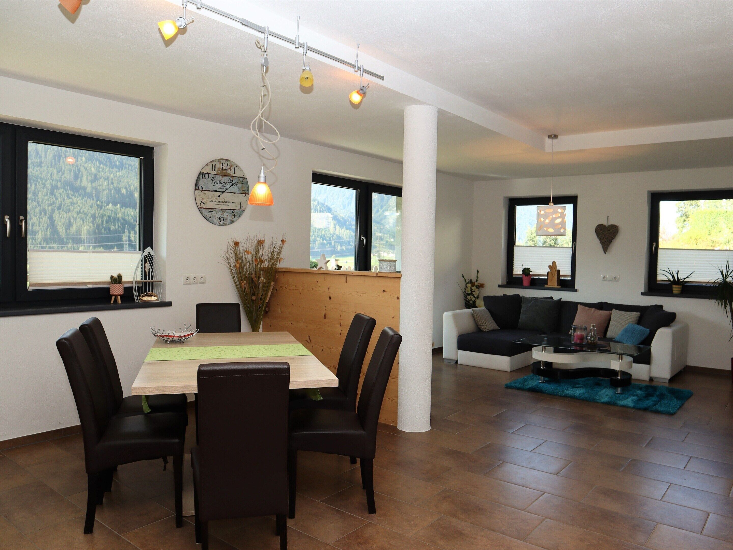 A modern living room with a dining area, large windows, and a view of the outdoors.