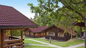 Un bâtiment de style cabane en bois, doté d’un toit en tuiles, entouré d’une zone herbeuse et d’arbres.
