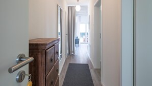 A narrow hallway with a wooden dresser, a metal handle door, and a dark mat on the floor. - Liebevoll Eingerichtete Ferienwohnung in Husum (Husum)