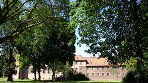 A large building with multiple windows and a red roof, surrounded by a well-maintained lawn and trees. - Liebevoll Eingerichtete Ferienwohnung in Husum (Husum)