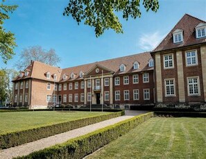 Een groot, historisch gebouw met symmetrische architectuur, veel ramen en een verzorgd gazon.