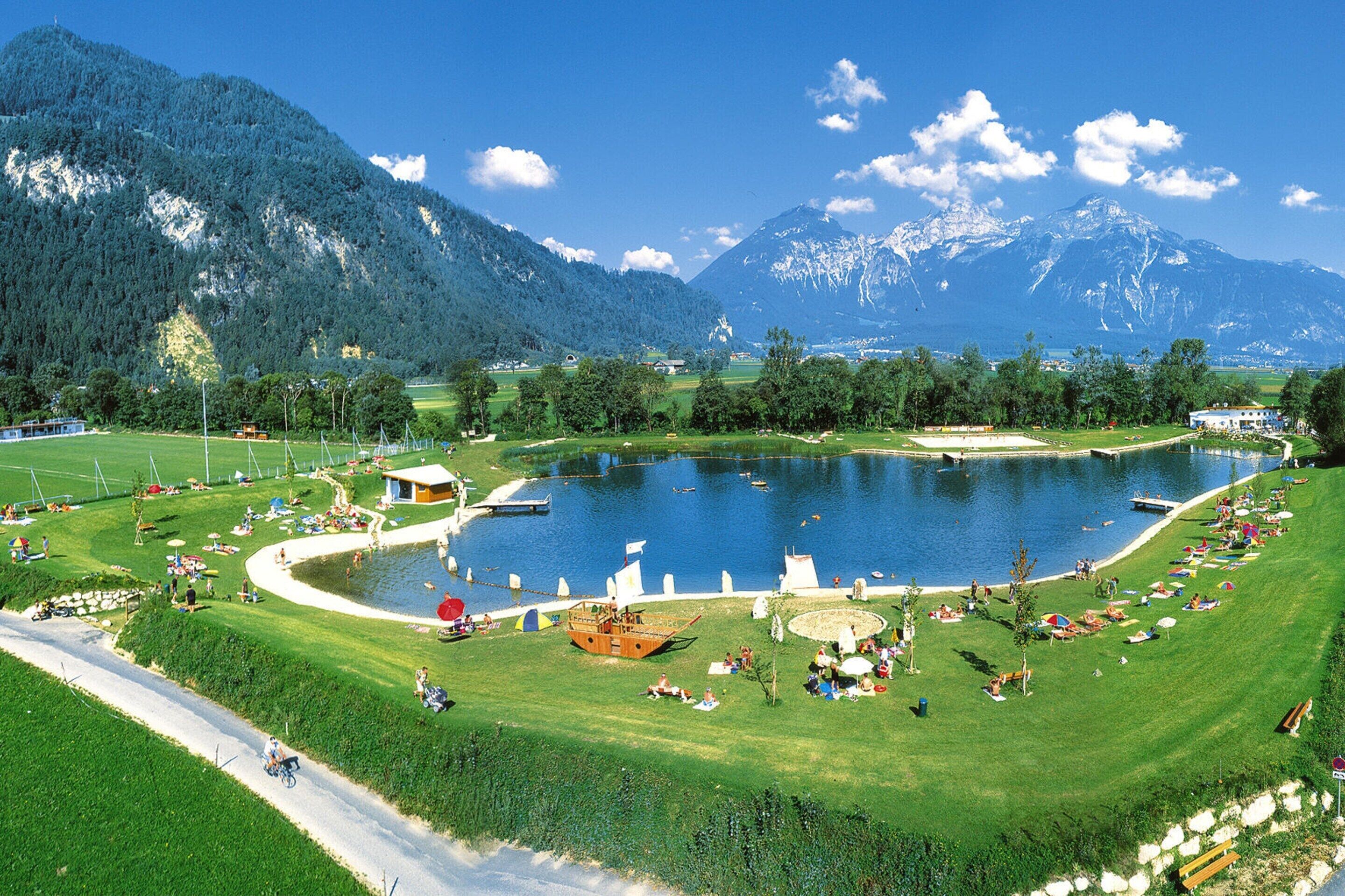 Un resort sul lago con un molo per barche, aree verdi e montagne sullo sfondo.