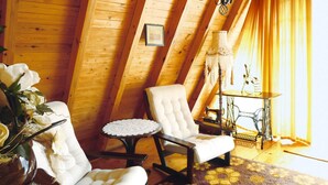 A cozy attic room with wooden walls, a white upholstered armchair, a small round table, and a sewing machine. - Holiday Home in Kashubia Near Lake (Suleczyno)