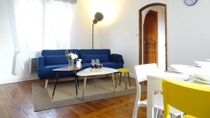 Ein Wohnzimmer mit einem blauen Sofa, einem runden Couchtisch, einem gelben Sessel und einem weißen Esstisch.