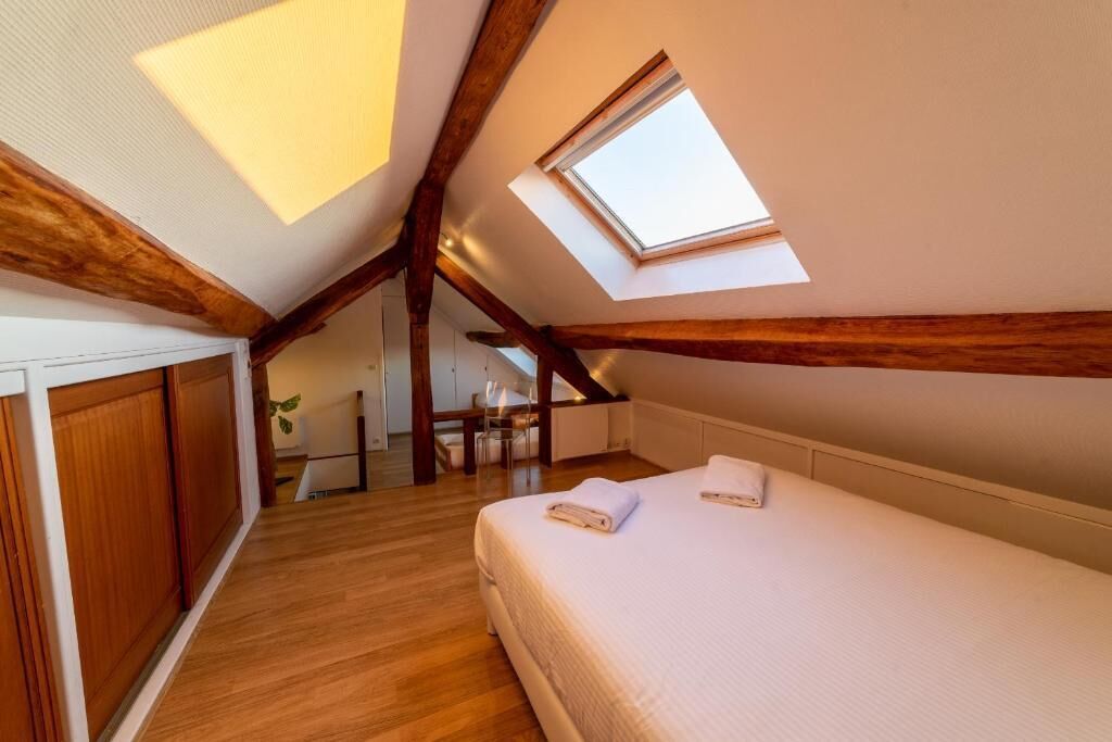 A bedroom with a skylight, wooden beams, a bed, and a small desk area.