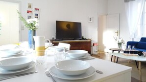 Ein modernes Wohnzimmer mit einem Esstisch für vier Personen, einem Flachbildfernseher und einem blauen Sofa.