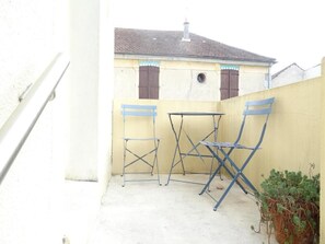 A small outdoor patio with a table and two chairs, a potted plant, and a building in the background. - Le Duplex - A 10 minutes de Disneyland (Montevrain)