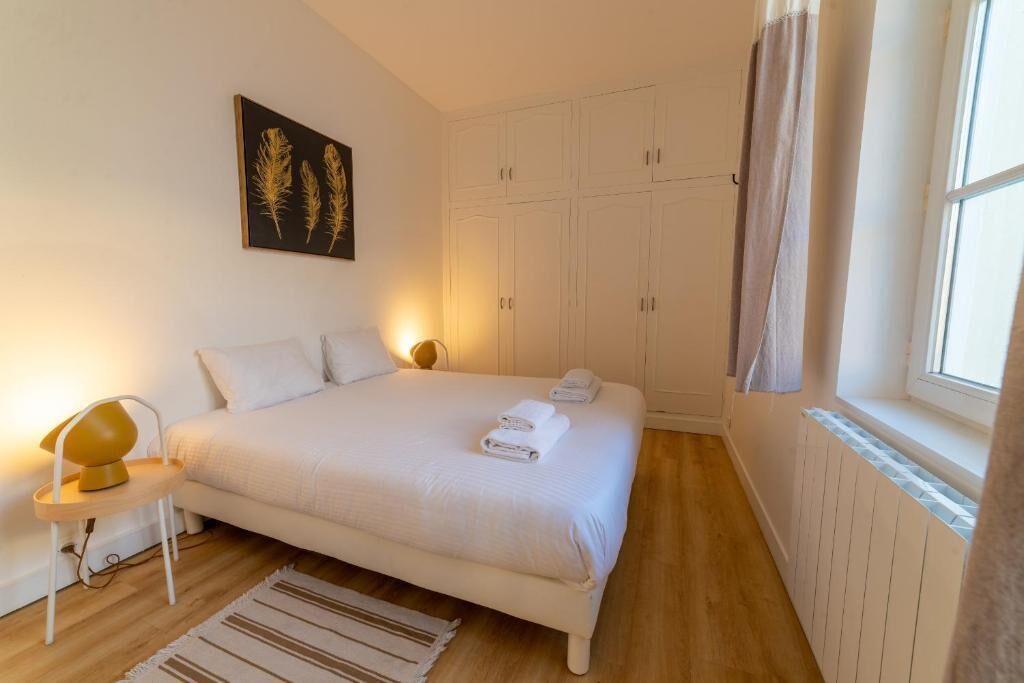 Une chambre à coucher avec un lit, une table de chevet avec une lampe, une fenêtre avec des rideaux et une armoire.