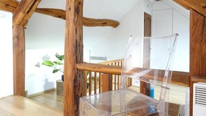 Ein Zimmer mit freiliegenden Holzbalken, einem klaren Kunststoffstuhl und einer weißen Wand mit einem Blumentopf.